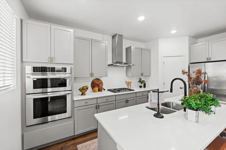 Kitchen featuring white cabinetry with gold-toned hardware, stainless steel appliances, a gas cooktop with a range hood, and a white subway tile backsplash