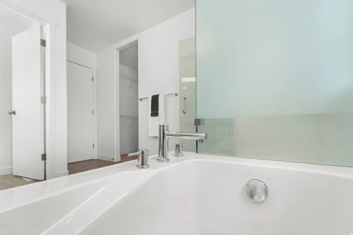 White soaking tub with chrome fixtures and a frosted glass shower partition