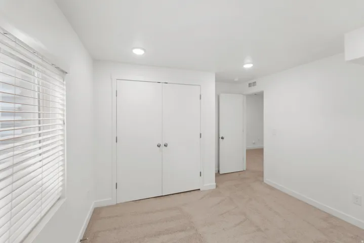 White walls with recessed lighting, light-colored carpeting, a window with horizontal blinds, and a double-door closet