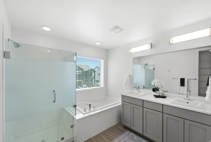 Spacious bathroom featuring a glass-enclosed shower, built-in bathtub, dual vanity with shaker-style cabinetry, and wood-finish flooring
