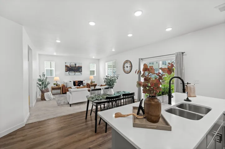 Recessed lighting, wood-finish flooring, white walls, kitchen island with dual basin sink, and a sliding glass door