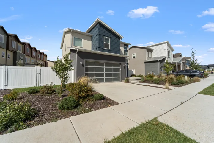 Modern architectural style featuring a multi-tone exterior, attached garage with frosted panel door, concrete driveway, and established landscape beds
