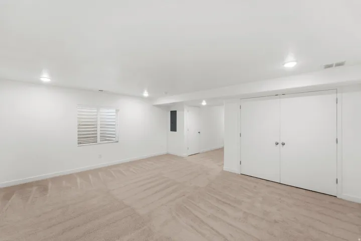 Recessed lighting illuminating neutral carpeting, white walls, and a window with horizontal blinds