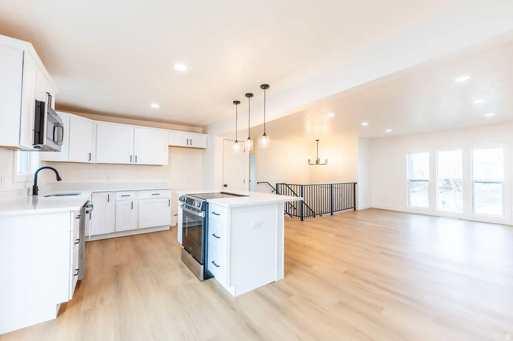 Open-concept living space featuring a kitchen island with pendant lighting, stainless steel range, and white cabinetry