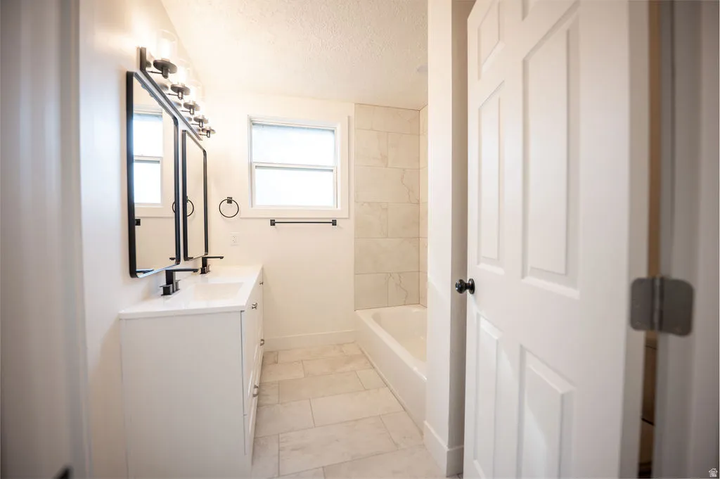 Dual vanity with white cabinetry and integrated sinks, matte black hardware, tiled flooring, and a tiled bath surround