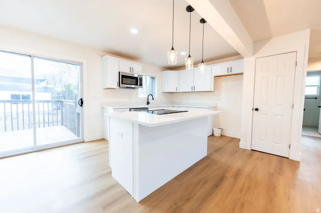 Modern kitchen featuring wood-finish flooring, white cabinetry, a kitchen island with built-in cooktop, and a sliding glass door opening to an outdoor deck