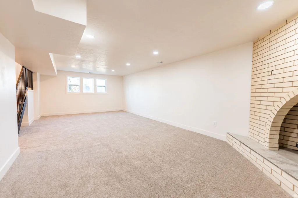 Recessed lighting, carpet flooring, three transom windows, a brick fireplace, and a staircase with metal railings
