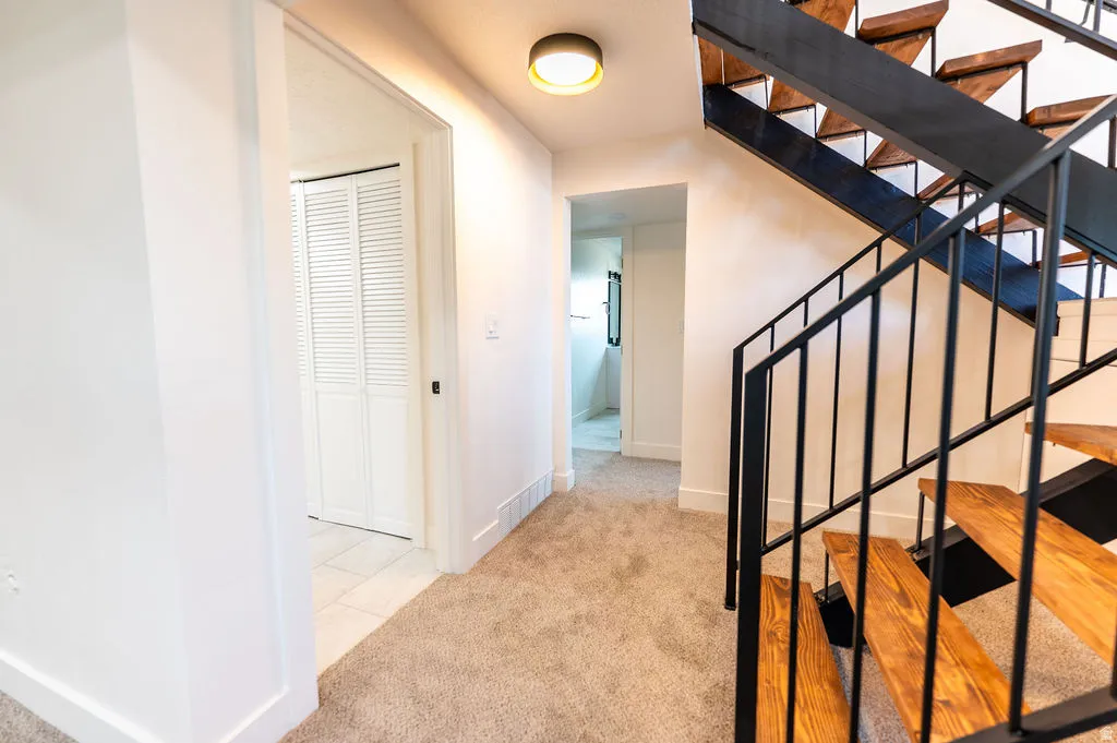 Open tread wood staircase with black metal railing, neutral carpeted flooring, white walls, and a contemporary ceiling light fixture