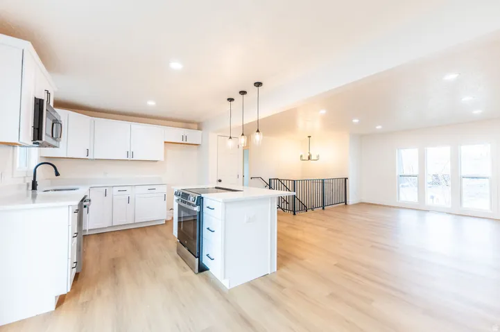 Open-concept living space featuring a kitchen island with pendant lighting, stainless steel range, and white cabinetry