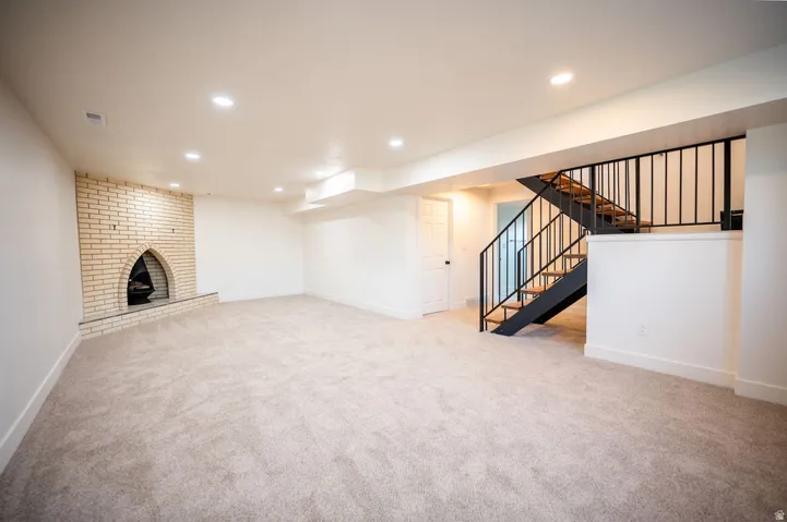 Spacious room with plush carpeting, recessed lighting, a brick fireplace, and an open-tread staircase with black metal railings