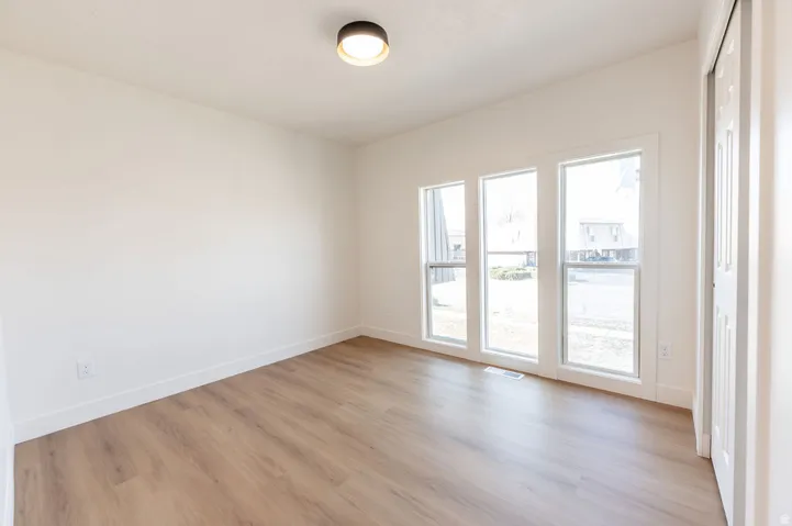 Vaulted ceiling with a flush-mount light fixture, wood-finish flooring, three vertical windows, and a bi-fold door
