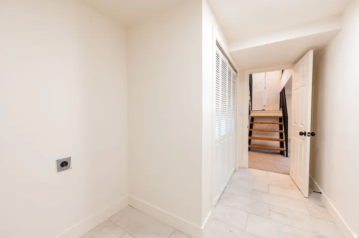 Laundry area with wall hookups, tile flooring, louvered bi-fold doors, and a wood staircase with carpeted landing