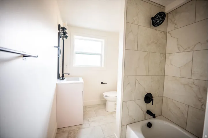 Tile-surround bathtub with matte black fixtures, single vanity with a rectangular sink, and light-toned floor tile