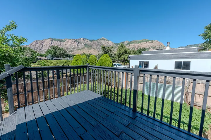 Deck with dark painted wood flooring and railing, overlooking a green lawn with a wood fence, featuring a mountain backdrop