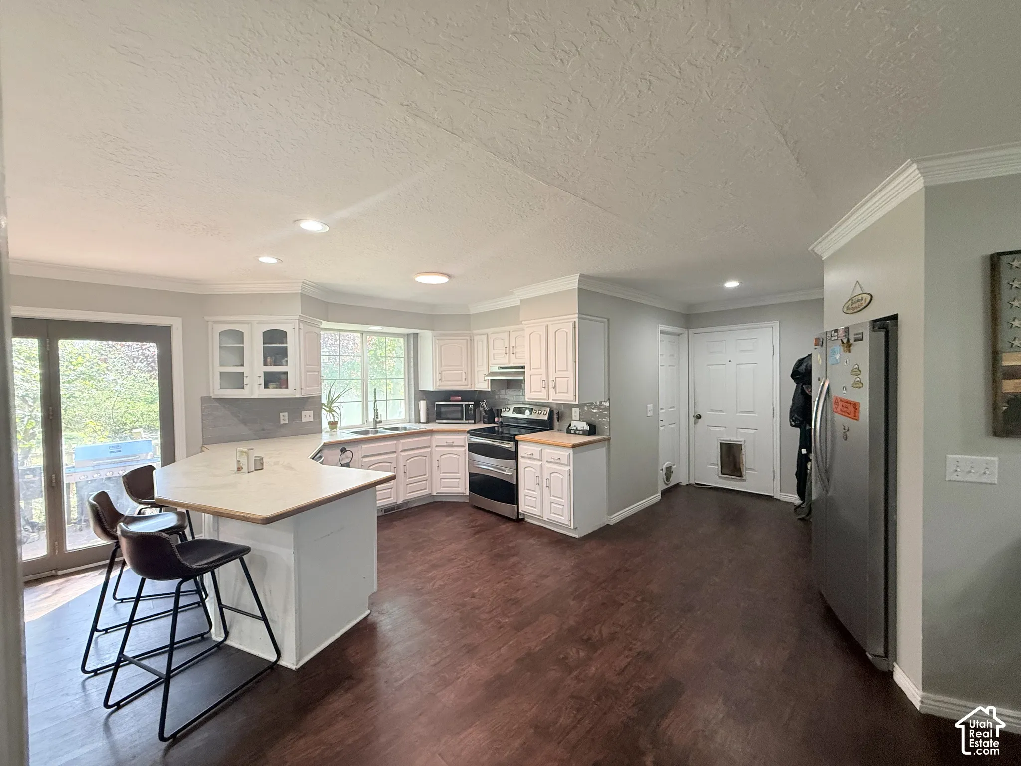 Kitchen featuring wood-finish flooring, white cabinetry, a kitchen island with seating, a large bay window, and stainless steel appliances