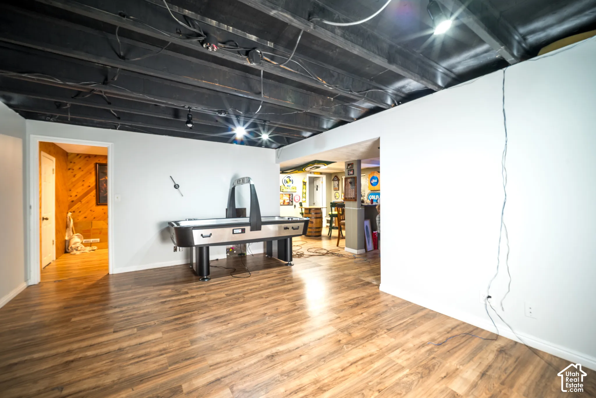 Open room with wood-finish flooring, white walls, and a painted exposed ceiling