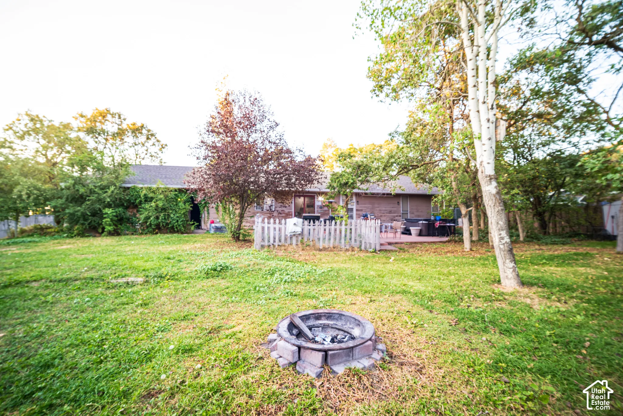 Expansive backyard with a stone-lined fire pit, mature trees, and a private patio area