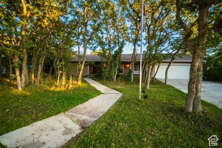 Mature trees providing natural shade, concrete walkway leading to the front entry, attached garage with a white door, and a flag pole