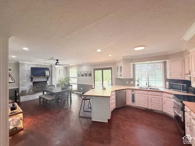 Open-concept living space featuring wood-finish flooring, a white-painted brick fireplace, recessed lighting, and a kitchen with white cabinetry