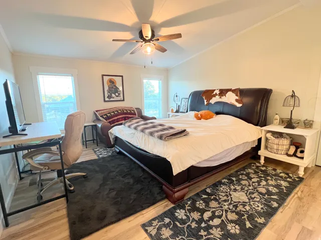 Vaulted ceiling, wood-finish flooring, ceiling fan with integrated lighting, multiple windows, and crown molding