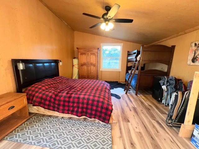 Vaulted ceiling, wood-finish flooring, ceiling fan with integrated lighting, natural light window, and wall-mounted light fixtures