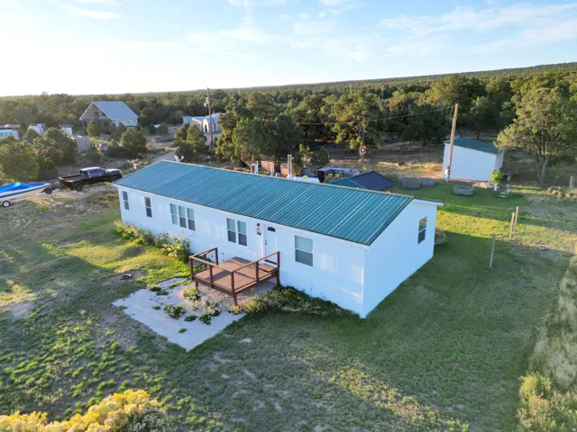 White exterior with a green metal roof, front wood deck, and surrounding natural landscape