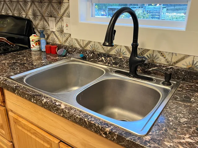 Dual basin stainless steel sink with a matte black gooseneck faucet, set within a patterned countertop, complemented by a decorative tile backsplash