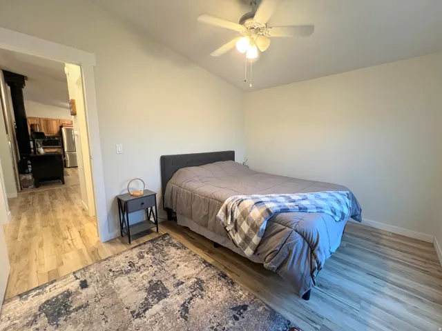 Vaulted ceiling with a ceiling fan, wood-finish flooring, and a doorway with white trim