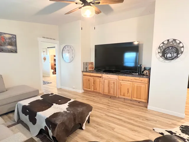Wood-finish flooring, built-in cabinetry with dark countertop, ceiling fan with integrated lighting, and white trim throughout