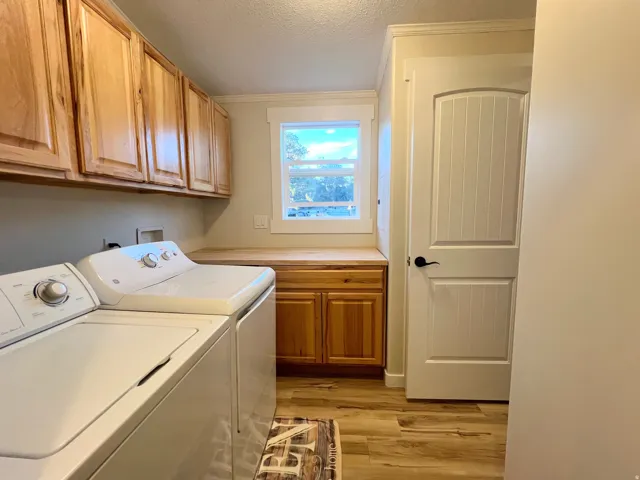 Laundry area featuring wood-finish flooring, natural wood cabinetry, a built-in wood-finish countertop, and a window with white trim