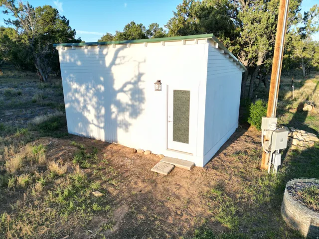White exterior structure with a green roof, single glass-paned entry door, and an exterior light fixture