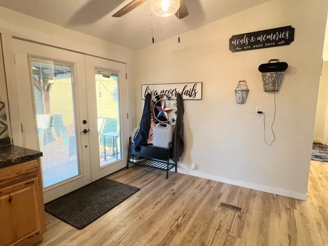 Dual glass-panel patio doors, wood-finish flooring, light wood cabinetry, dark speckled countertop, and a ceiling fan with integrated lighting