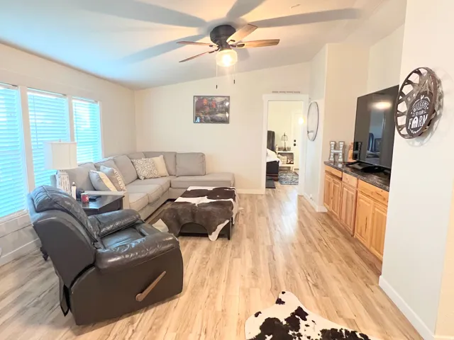 Vaulted ceiling with a ceiling fan, wood-finish flooring, multiple windows with blinds, and built-in cabinetry with a dark countertop