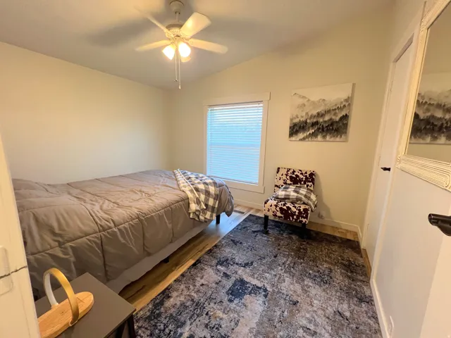 Wood-finish flooring with accent rug, overhead ceiling fan, and window with blinds