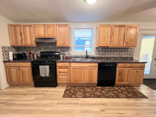 Kitchen featuring wood-finish cabinetry, dark countertops, a tile backsplash, black appliances, and wood-finish flooring