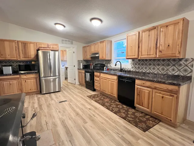Kitchen featuring wood-finish flooring, wood cabinetry, patterned tile backsplash, stainless steel refrigerator, and black appliances