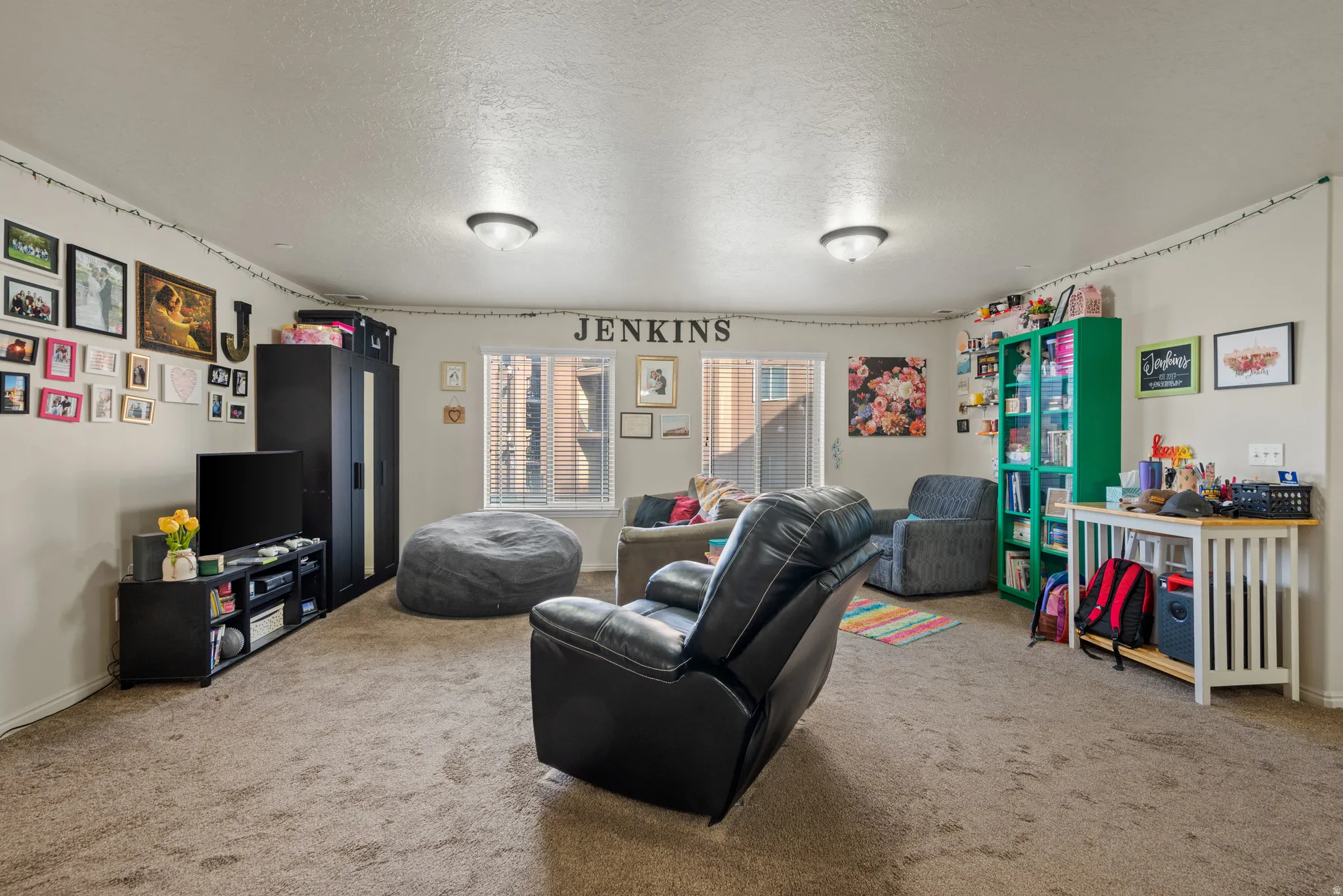 Carpeted room featuring a window with blinds, wall-mounted light fixtures, and a textured ceiling