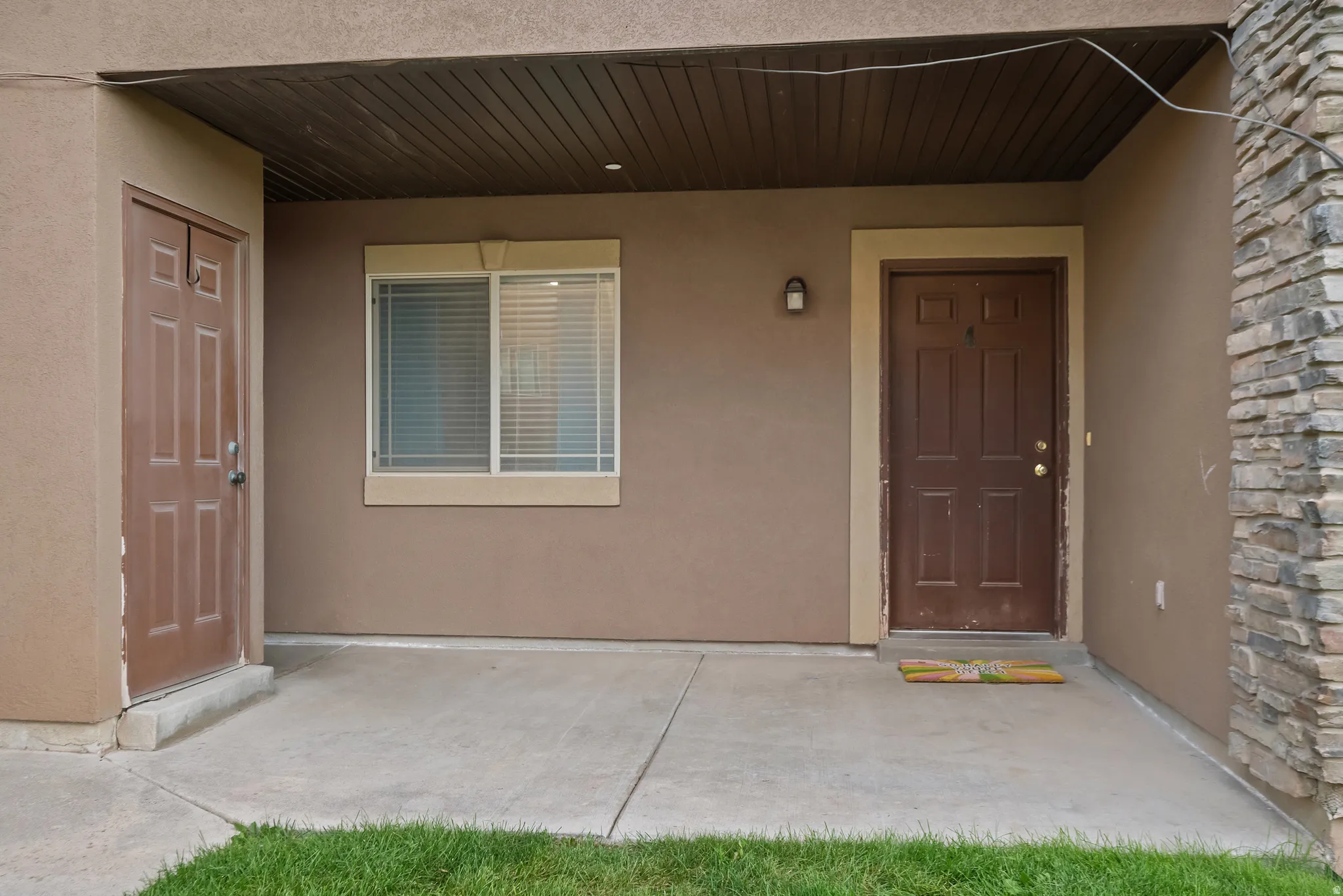 Covered entry with concrete patio, two paneled doors, exterior wall sconce, and stacked stone accent