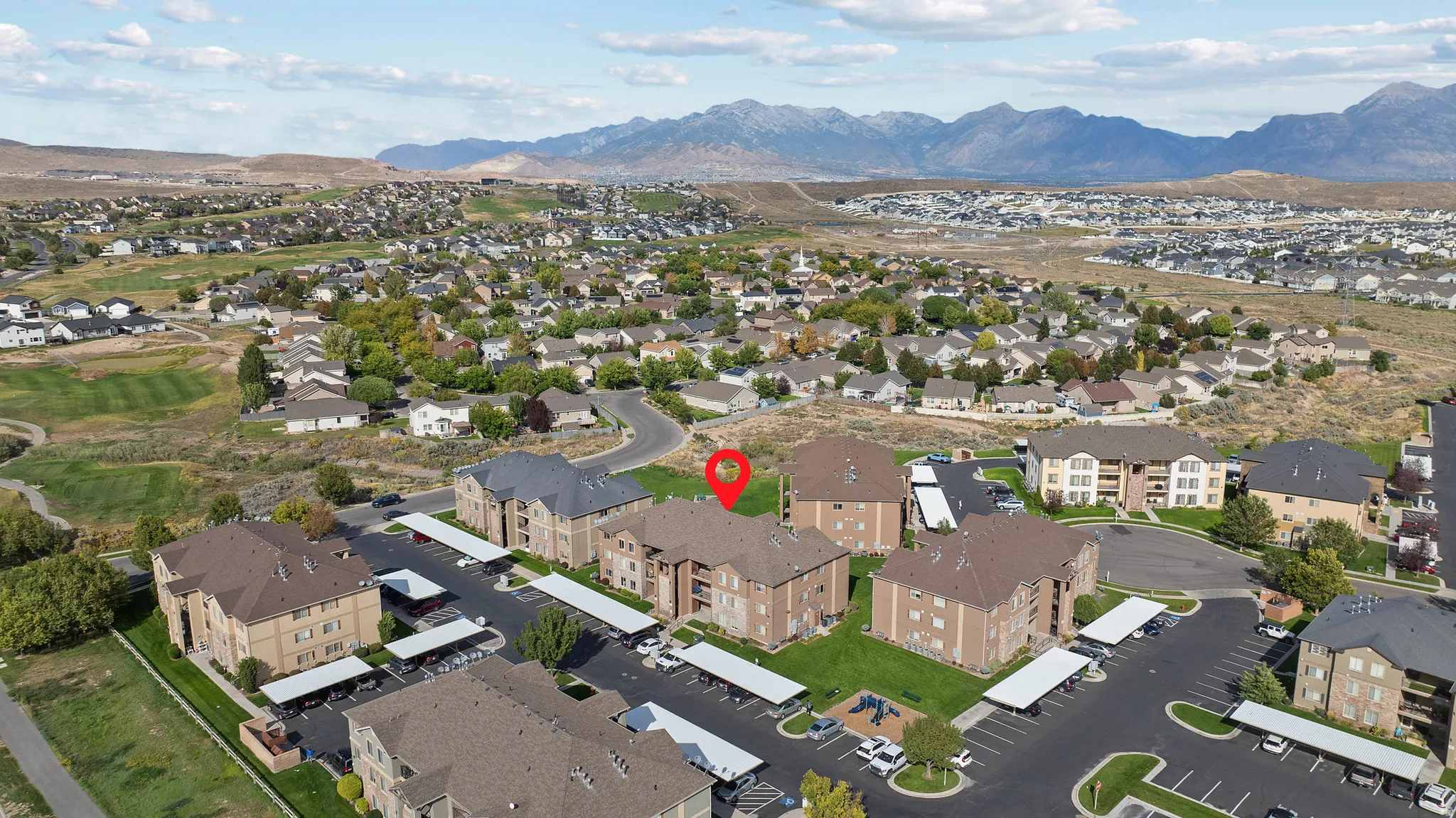 Multi-story residential buildings with covered parking, surrounded by green spaces and distant mountains