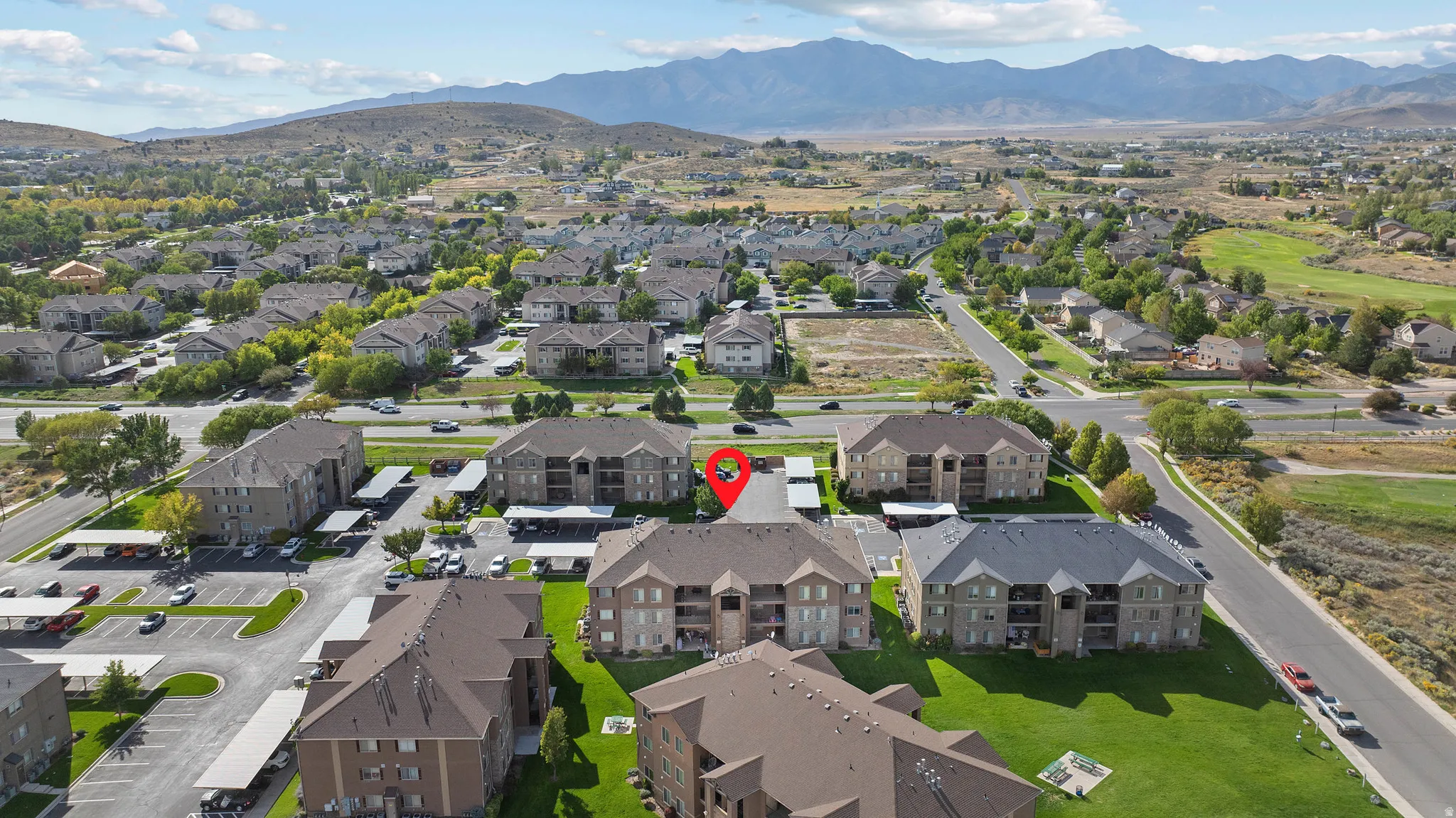 Expansive aerial perspective showcasing multi-story residential buildings, paved parking areas, and surrounding green spaces