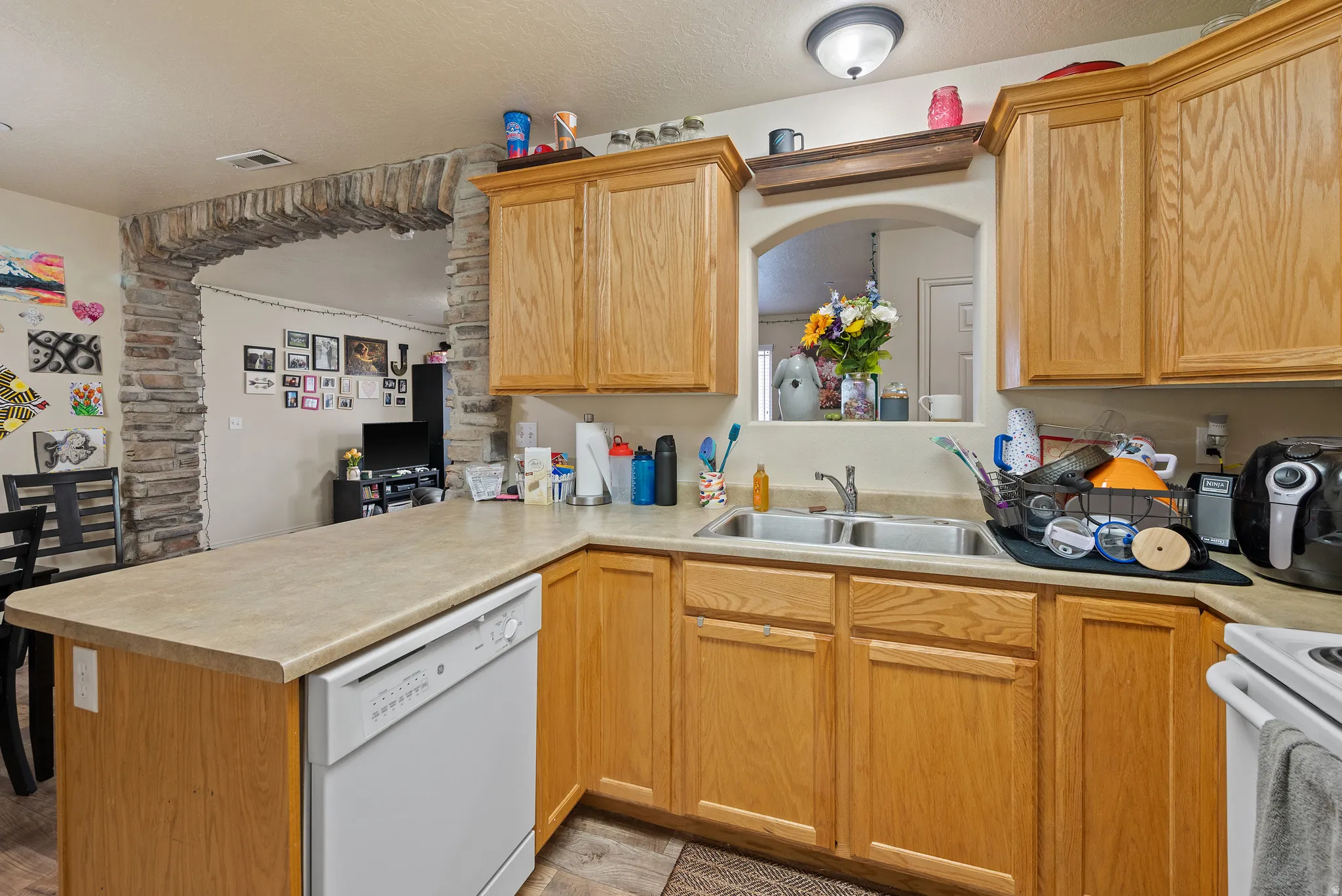 Kitchen featuring light wood-finish cabinetry, a built-in dishwasher, and a double basin stainless steel sink
