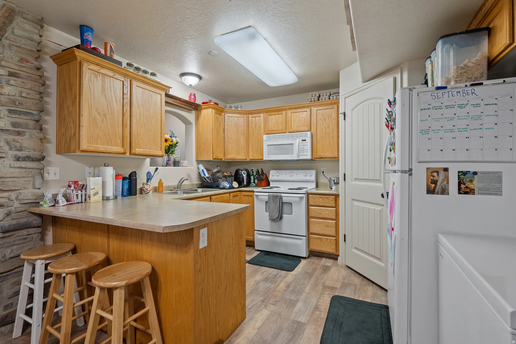 Kitchen featuring wood-finish flooring, wood cabinetry, white appliances, a stone accent wall, and a curved countertop with seating