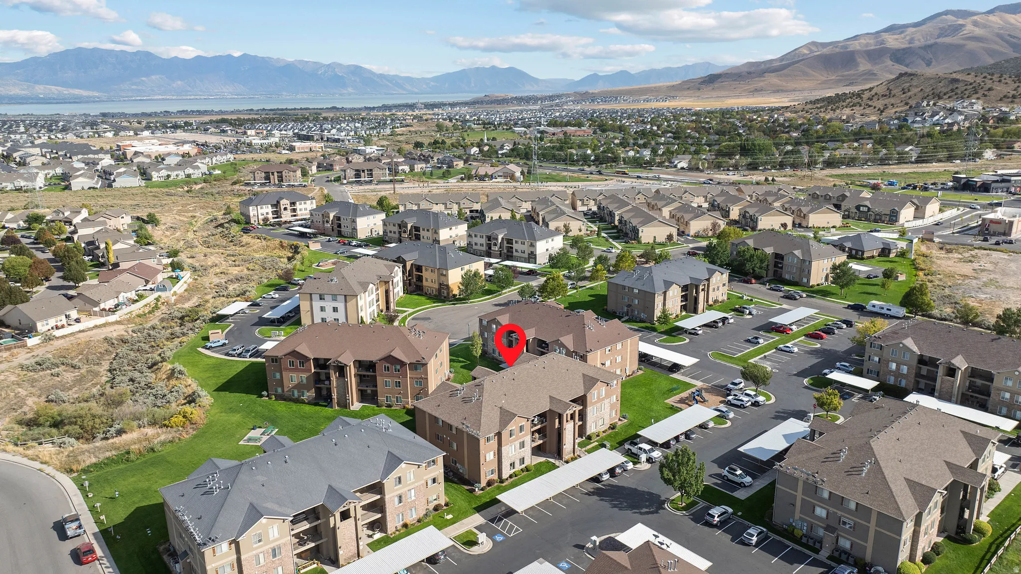 Apartment complex with covered parking, surrounded by green spaces and distant mountain ranges