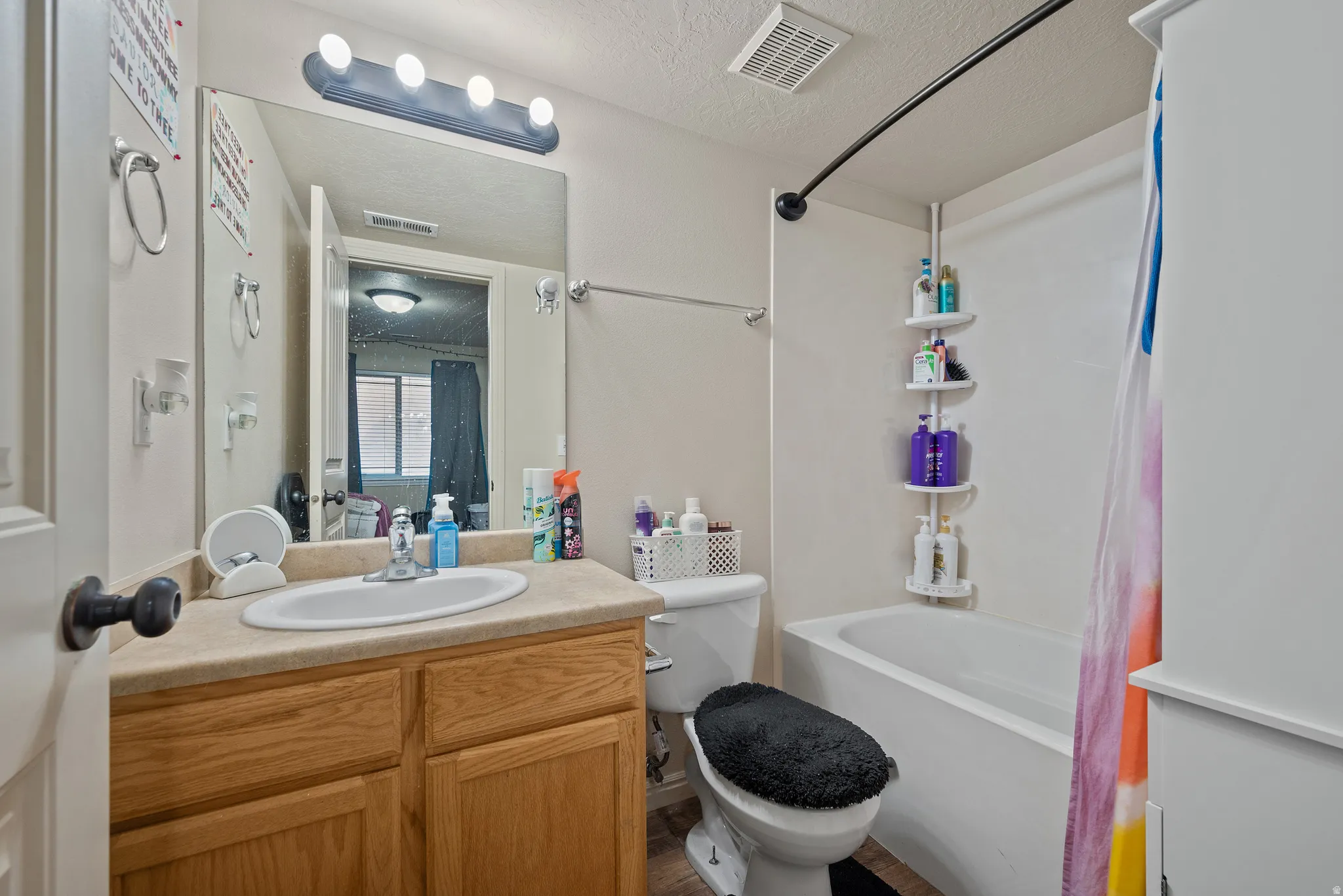 Bathroom featuring a wood-finish vanity with an integrated sink, a full-width wall mirror, and a bathtub with a shower
