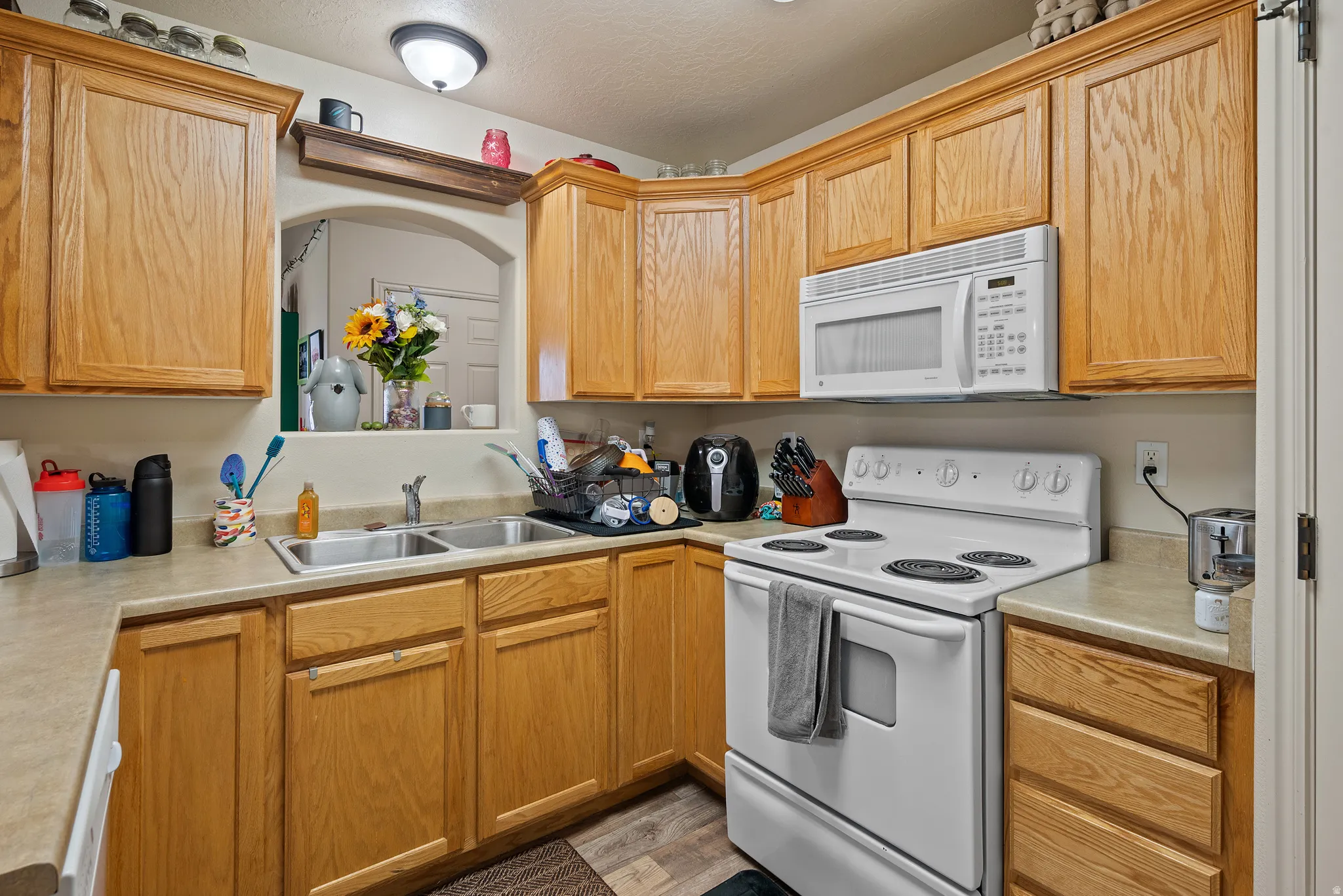 Wood-finish cabinetry, solid surface countertops, double basin sink, white range, and built-in microwave