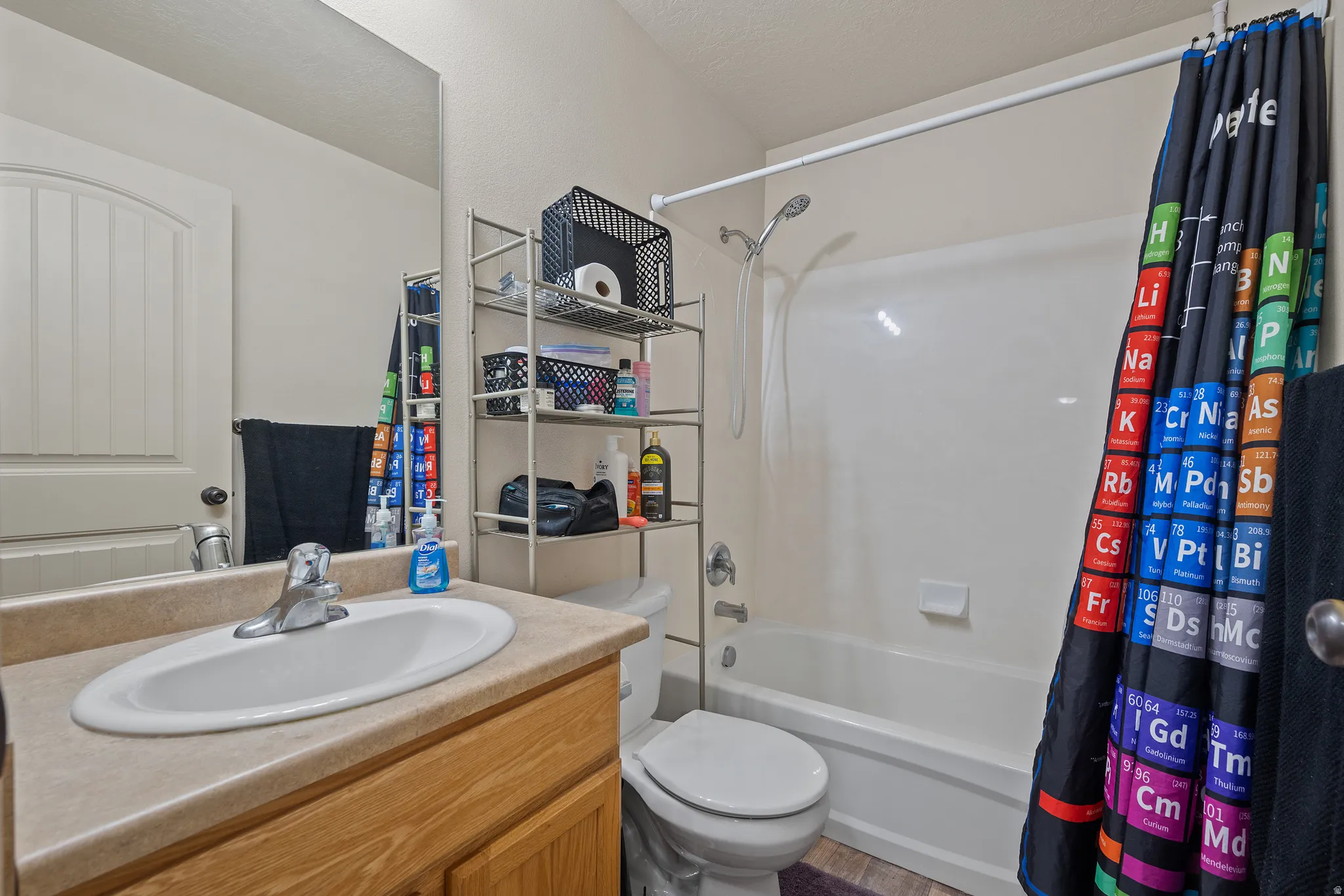 Bathroom featuring a single vanity with an integrated sink, wood-finish cabinetry, a full-width mirror, and a shower-over-tub combination