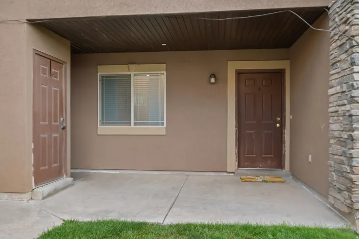 Covered entry with concrete patio, two paneled doors, exterior wall sconce, and stacked stone accent