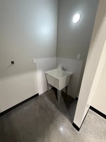 Utility sink with a chrome faucet, concrete flooring, and an overhead light fixture