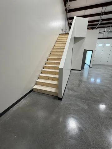 Polished concrete flooring, exposed ceiling joists, and a partial second-story staircase