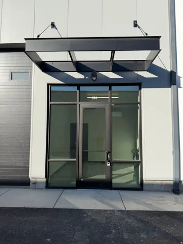 Modern storefront entrance with full-light glazing, a steel-framed awning, and a roll-up door